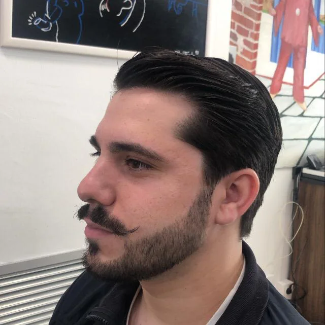 Peinado hacia atrás con barba perfilada y bigote definido
